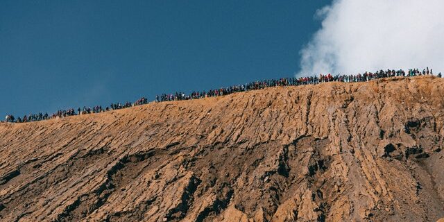 Bottom up view of a large exposed slope of a hill with people standing along the top